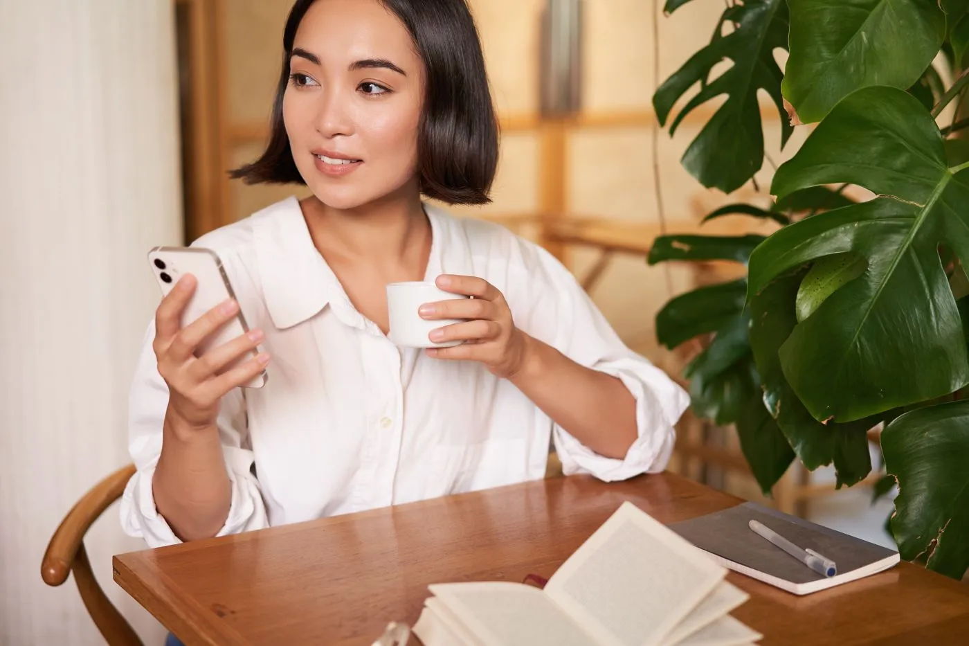 A woman holding a phone reading a meeting summary in chat at a cafe table